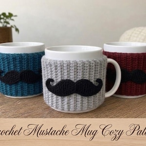 May include: Three white ceramic mugs, each wrapped in a ribbed crochet cosy. The cosies are teal, light grey, and dark red, and each features a black crocheted moustache appliqué centred on the front. The text Crochet Mustache Mug Cozy Pattern is visible.
