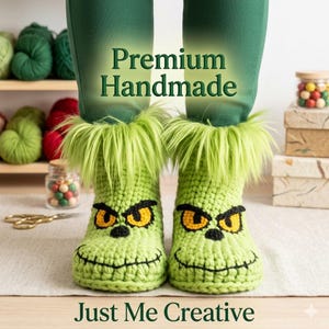 May include: Handmade green crochet boots with a Grinch face design, featuring yellow eyes, a black nose, and a smiling mouth. The boots have a fluffy green trim. The text "Premium Handmade" and "Just Me Creative" are visible.