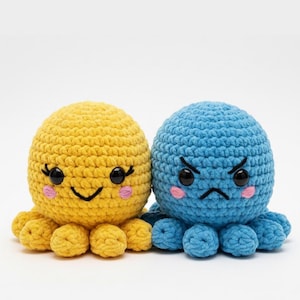 Puede incluir: Dos juguetes de pulpo de ganchillo. Uno es amarillo con una cara sonriente y mejillas rosas. El otro es azul con una cara enfadada y mejillas rosas. Ambos tienen ojos negros y tentáculos.