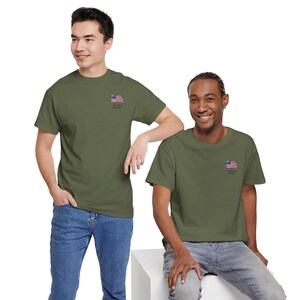 Puede incluir: Dos personas vistiendo camisetas verde oliva con un pequeño diseño de la bandera estadounidense y las palabras "America Strong" bordadas en el pecho. Las camisetas se combinan con vaqueros azules.