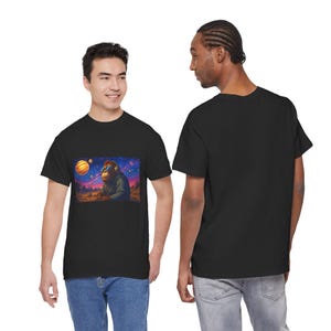 May include: Black t-shirt featuring a colorful graphic of an orangutan wearing headphones and sunglasses, set against a cosmic landscape with planets and stars. The orangutan is wearing a hoodie.