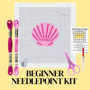 May include: A beginner needlepoint kit featuring a pink seashell design. The kit includes pink embroidery floss, a needle, scissors, a pen, and a stitch guide. The words "BEGINNER NEEDLEPOINT KIT" are printed at the bottom.