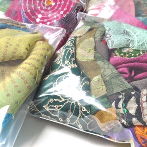 May include: Assortment of colorful fabric scraps in clear plastic bags. The fabrics are a mix of textures, including lace, sequins, and embroidery.