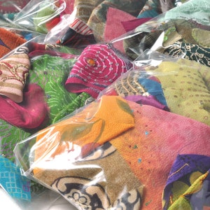 May include: A collection of colorful fabric scraps in various patterns and textures are packaged in clear plastic bags. The fabrics include green, pink, orange, blue, and gold.