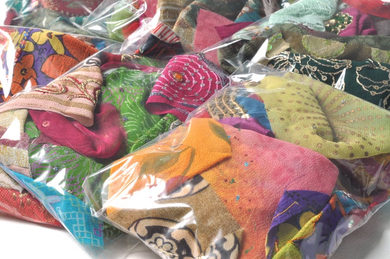 May include: A collection of colorful fabric scraps in various patterns and textures are packaged in clear plastic bags. The fabrics include green, pink, orange, blue, and gold.