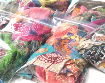 May include: Assortment of colourful fabric scraps in clear plastic bags. The fabric scraps are a mix of patterns and textures, including floral, geometric, and paisley designs.