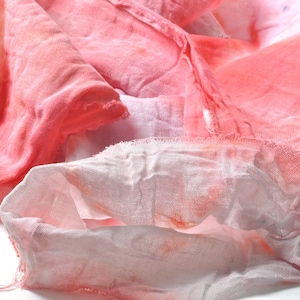 May include: Close-up of soft, textured fabric in shades of pink and white. The fabric appears to be layered and slightly crumpled, with a delicate, airy quality. The color transitions create a watercolor effect.