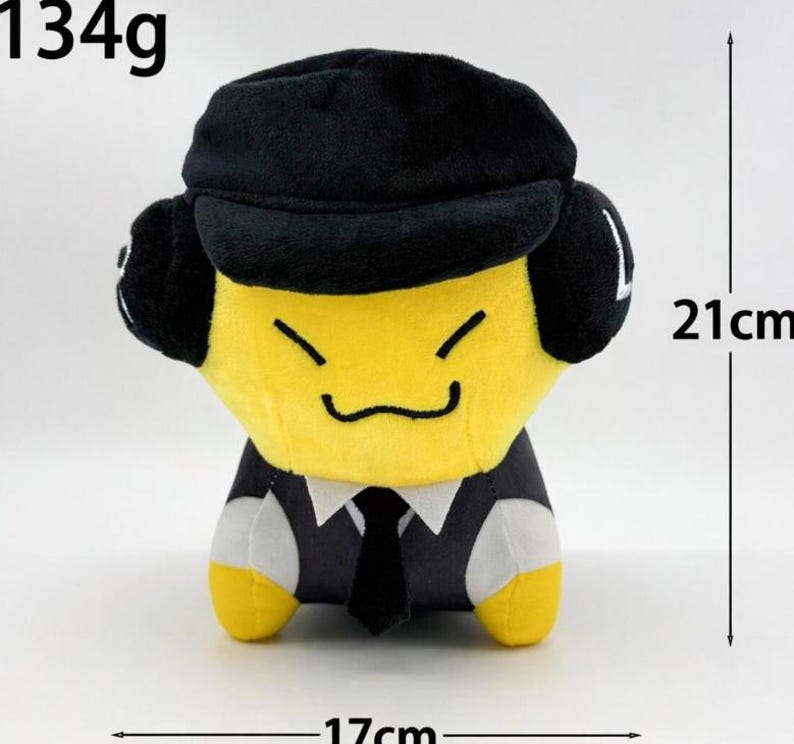 May include: A plush toy with a yellow face, black hat, and a black suit with a tie. The toy is 21cm tall and 17cm wide, weighing 134g. The toy has a smiling face.