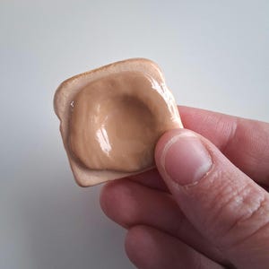 Puede incluir: Una pequeña rebanada de pan tostado con una generosa capa de mantequilla de cacahuete. La tostada tiene una corteza marrón claro y un centro de color beige. La mantequilla de cacahuete es de un marrón cremoso.