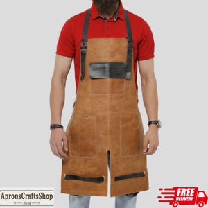 Könnte beinhalten: Eine braune Lederschürze mit schwarzen Akzenten, mit einer Brusttasche und zwei unteren Taschen. Die Schürze hat schwarze Riemen und ein geteiltes Design am unteren Ende. Der Text "ApronsCraftsShop" ist ebenfalls sichtbar.
