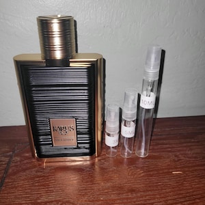 May include: A rectangular black and gold perfume bottle with a ribbed texture and a gold cap, labeled Karus Gold Absolu. Beside it are three clear glass spray sample vials with white labels marked 3ml, 5ml, and 10ml, featuring clear plastic caps.