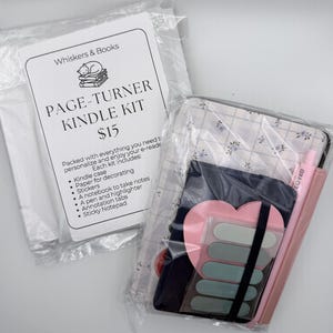 May include: A Page-Turner Kindle Kit in clear plastic packaging. The kit includes a white information card with a cat illustration, a floral patterned e-reader case, a dark notebook, a pink pen, a heart-shaped sticky note, and green tabs.