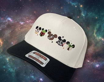May include: A white baseball cap with a black brim featuring embroidered cartoon character designs. The designs include characters from a popular science fiction franchise. The cap has a curved brim and a structured crown.
