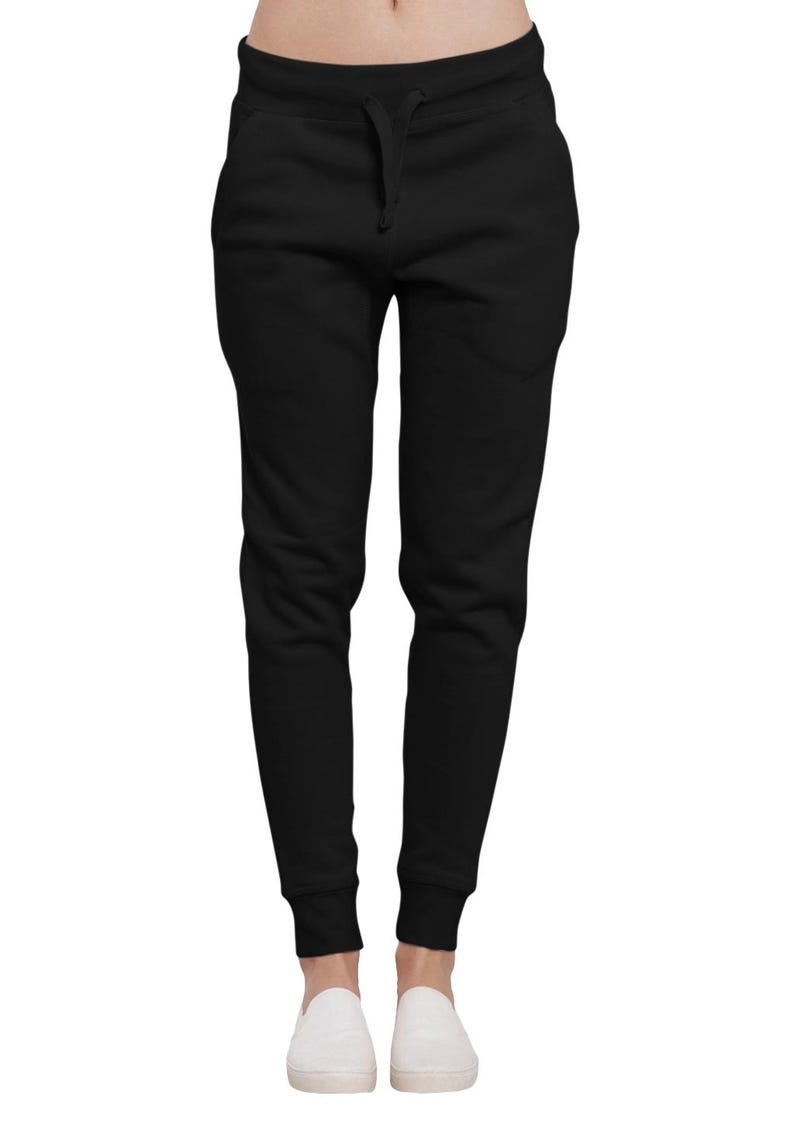 May include: Black sweatpants with a drawstring waist and elastic cuffs. The pants have two front pockets and are paired with white slip-on shoes. The casual pants are made of a soft material.