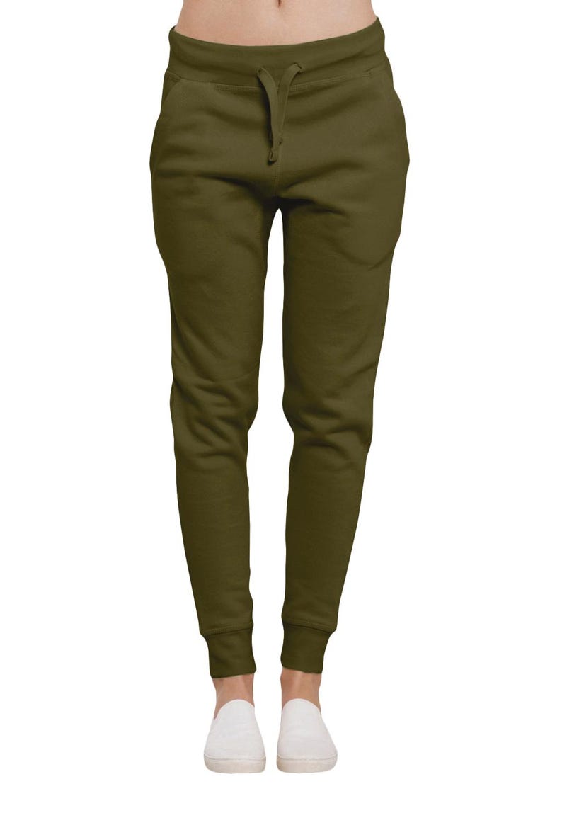 May include: Olive green sweatpants with a drawstring waist and elastic cuffs. The pants have two front pockets and are made of a soft, comfortable material. The model is wearing white slip-on shoes.