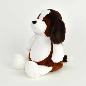 May include: A plush stuffed dog toy in a sitting position. The toy features a brown and white color scheme, with brown ears and patches, and white accents on the chest, paws, and tail. The dog has a black nose and is set against a white background.