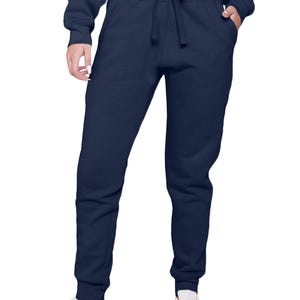 May include: Navy blue sweatpants with a drawstring waist and pockets. The pants are cuffed at the ankles and paired with white sneakers. The model is also wearing a matching navy blue cropped sweatshirt.