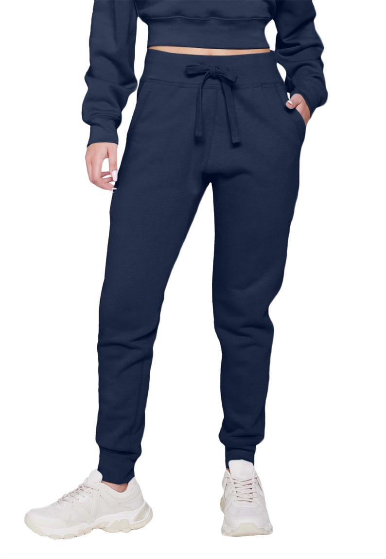 May include: Navy blue sweatpants with a drawstring waist and pockets. The pants are cuffed at the ankles and paired with white sneakers. The model is also wearing a matching navy blue cropped sweatshirt.