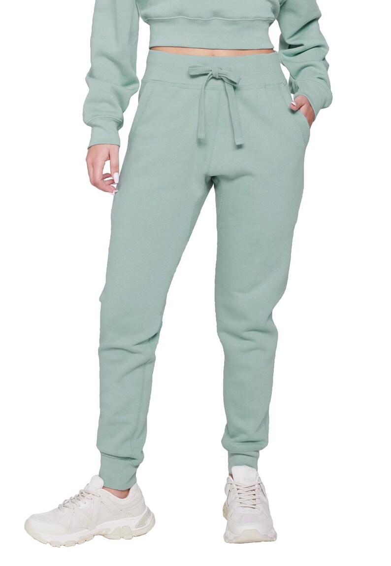 May include: A light green sweat suit, including a crew neck sweatshirt and matching sweatpants. The sweatpants have a drawstring waist and cuffed ankles. White sneakers complete the casual outfit. The clothing is made of a soft, comfortable material.