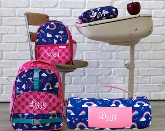 May include: A set of two backpacks, a pencil case, and a nap mat, all featuring a dark blue fabric with a colorful rainbow and cloud pattern. Each item is personalized with the name Lizzy in white script and includes bright pink accents.