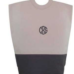 May include: A beige and dark gray canvas tote bag with a large, round, wooden handle. The bag has a monogram of the letters "CBS" in a circle on the front.