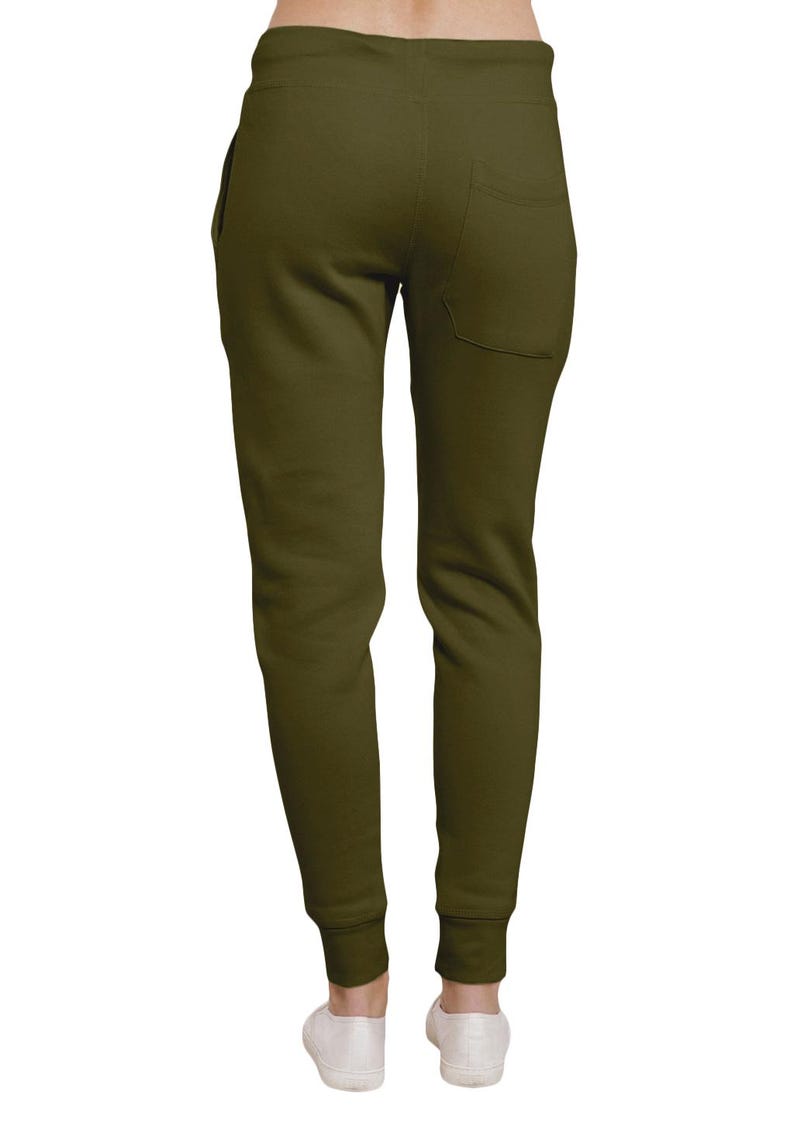 May include: Olive green sweatpants with a back pocket and elastic cuffs. The pants are shown from the back, with white shoes visible at the bottom. The material appears to be soft and comfortable.