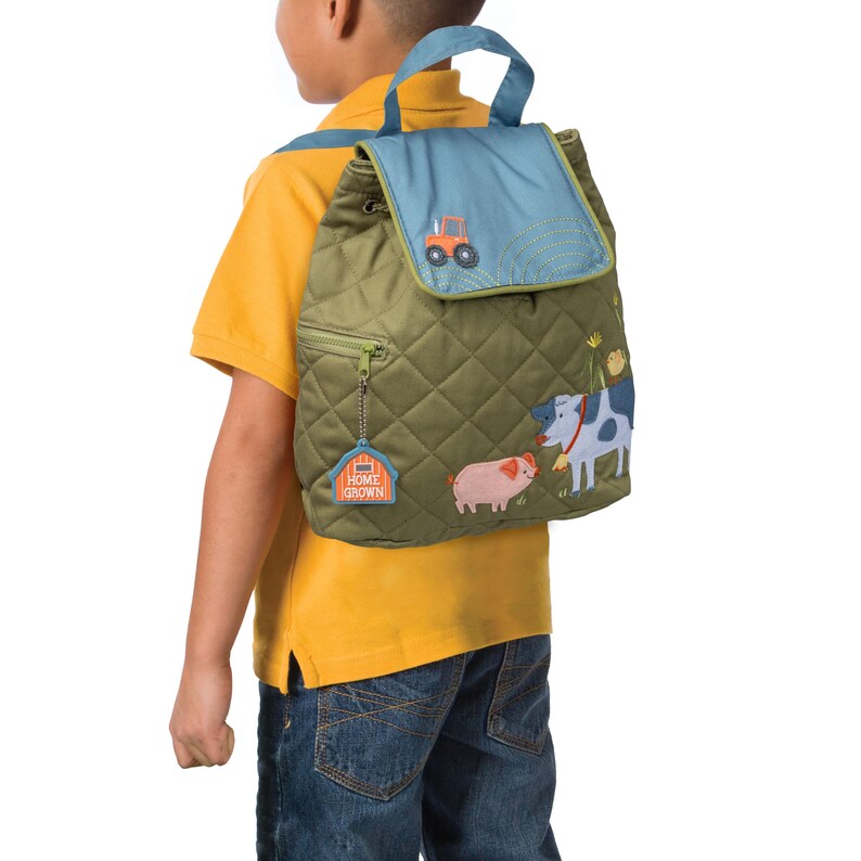 May include: A green quilted backpack with a blue flap and a drawstring closure. The backpack features embroidered farm animals, a tractor, and the text "Home Grown".
