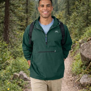 May include: A dark green hooded pullover jacket with a quarter-zip closure, a front zippered pocket, and the letters JAL embroidered in white on the chest. The jacket features long sleeves with elastic cuffs and is worn over a light blue shirt.
