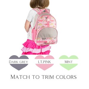 May include: Pink dinosaur backpack with a grey and white striped pocket. The backpack has a light pink trim and a mint green trim.  "MATCH TO TRIM COLORS" is written below the backpack.