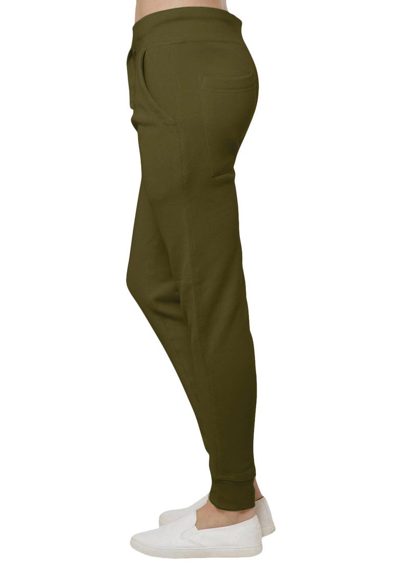 May include: Olive green joggers with a relaxed fit, featuring a front pocket and elastic cuffs. The pants are paired with white slip-on shoes, creating a casual and comfortable look. The fabric appears to be a soft, knit material.