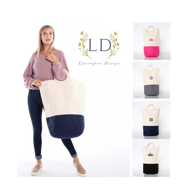 May include: A woman is holding a large canvas laundry hamper with a white top and a navy blue bottom. The hamper has two handles and is a great way to store laundry. There are four other laundry hampers in the image, each with a different color and design. The hampers are all made of canvas and have a white top and a colored bottom. The hampers are all available in a variety of colors and designs.