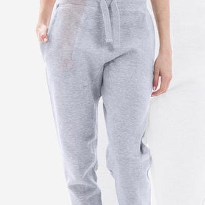 May include: Light gray sweatpants with a drawstring waist and pockets. The pants are made of a soft, comfortable material, perfect for casual wear. The image shows the pants from the waist down, with a person's hands in the pockets.