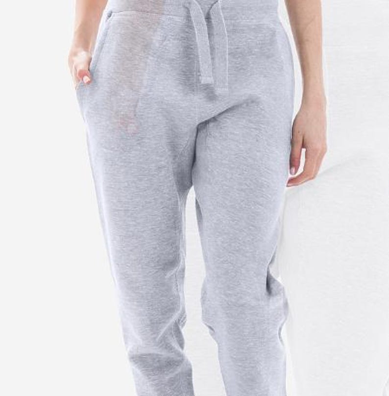 May include: Light gray sweatpants with a drawstring waist and pockets. The pants are made of a soft, comfortable material, perfect for casual wear. The image shows the pants from the waist down, with a person's hands in the pockets.