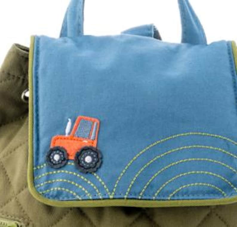 May include: A green quilted backpack with a blue flap featuring an orange tractor applique. The flap has green stitching around the edges and a small pocket with a zipper.