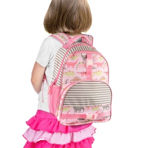 May include: A pink and grey backpack with a dinosaur print. The backpack has a front pocket and adjustable straps.