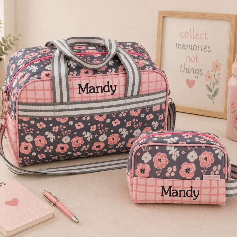 May include: A dark gray duffel bag and a matching smaller pouch, both featuring a pink floral pattern and a pink grid design. Each item is personalized with the name Mandy in black text. The bags have gray and white striped fabric handles.