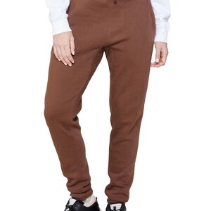May include: Brown sweatpants with a drawstring waist. The pants are a solid color and have a relaxed fit. The person is wearing black and white sneakers.