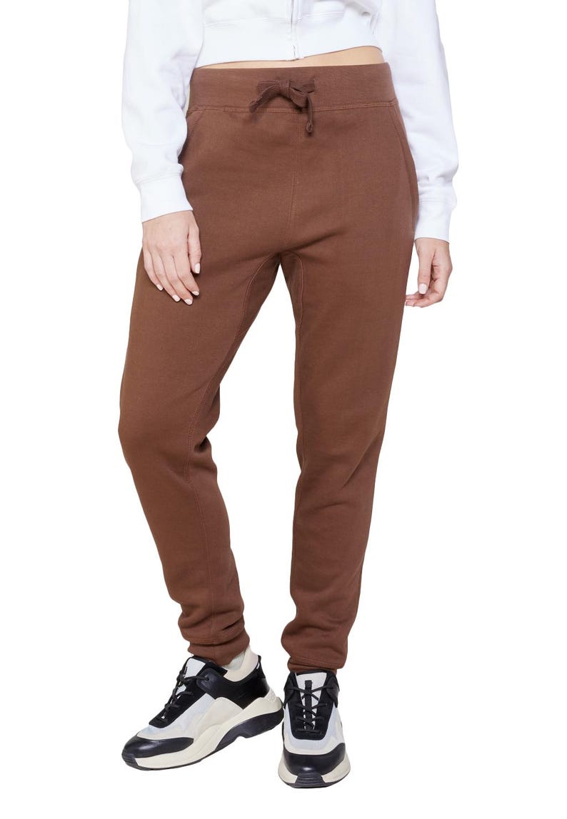 May include: Brown sweatpants with a drawstring waist. The pants are a solid color and have a relaxed fit. The person is wearing black and white sneakers.
