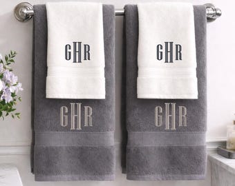 May include: Two sets of layered bath towels hanging on a metal rack. Each set includes a large dark gray towel and a smaller white hand towel. Both towels feature the embroidered monogram GHR in a serif font, with dark gray on white and light gray on dark gray.
