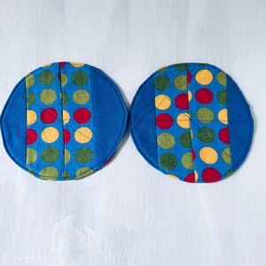May include: Two circular fabric coasters featuring a blue background with a central vertical panel of multicolored polka dots in red, yellow, and olive green. The coasters are quilted with visible stitching and have solid blue fabric borders.