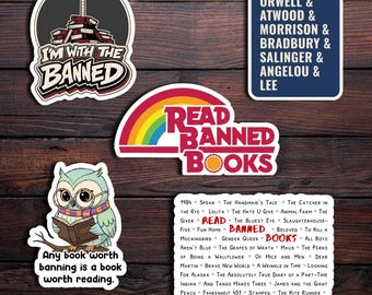 May include: A collection of stickers with literary themes. One sticker reads "I'm with the Banned" with a guitar on top of books. Another says "Read Banned Books" with a rainbow. Other stickers list authors and banned books.