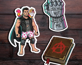 May include: Three stickers featuring a muscular character in a leather vest and heart-patterned boxers with a cat on their shoulder, a metallic gauntlet with the text YOU WILL NOT BREAK ME, and a brown book with a red anarchy symbol on the cover.