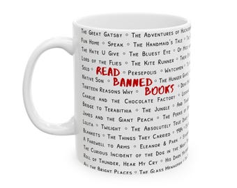 May include: A white ceramic mug featuring a list of book titles printed in black text. The words READ BANNED BOOKS are printed in large red letters in the center. The list includes titles such as The Great Gatsby, 1984, and Lolita.