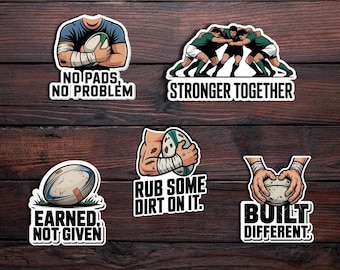 May include: Set of five rugby-themed stickers with motivational phrases. Designs include a player holding a ball, a team huddle, and hands with a ball. Phrases: "No Pads, No Problem", "Stronger Together", "Earned, Not Given", "Rub Some Dirt On It", and "Built Different".