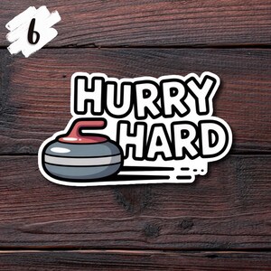 May include: A sticker featuring a curling stone graphic with the words "HURRY HARD" in bold, white letters. The curling stone is gray, red, and white. A white number 6 is in the upper left corner. The background is a dark wood grain.