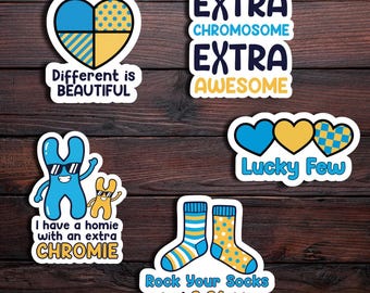 May include: A collection of colorful stickers with positive messages and graphics. Designs include a heart with blue and yellow patterns, the text "Different is Beautiful," and the phrase "Extra Chromosome Extra Awesome."