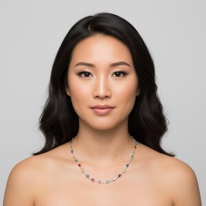 May include: A silver necklace with colorful gemstones. The necklace features a series of round, multi-colored gemstones, including red, green, blue, and yellow, set along a delicate silver chain. The woman in the image is wearing the necklace.