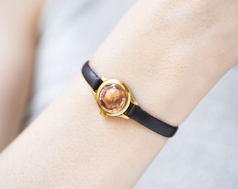 May include: A gold-tone wristwatch with a pink face and a black leather band.