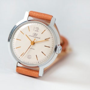 May include: A silver wristwatch with a white face and gold hands. The watch has a brown leather band and the words "ЧacOBHИK" and "СДЕЛАНО В СССР" are printed on the face.