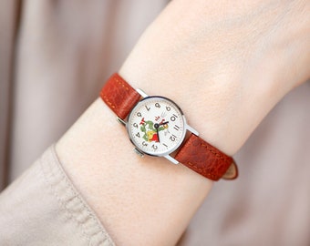 Peut inclure: Une montre-bracelet argentée avec un cadran blanc et un bracelet en cuir marron. Le cadran de la montre présente une illustration de dessin animé d'un coq et d'une poule.